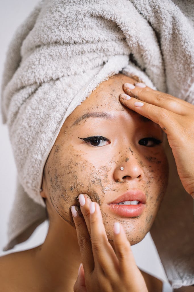 A Woman Wearing Hair Towel Applying homemade face Scrub on Her Face while Looking at the Camera