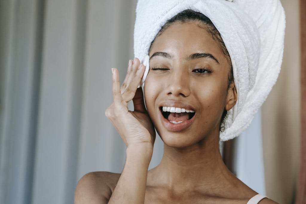 Happy ethnic woman wiping face with organic toners