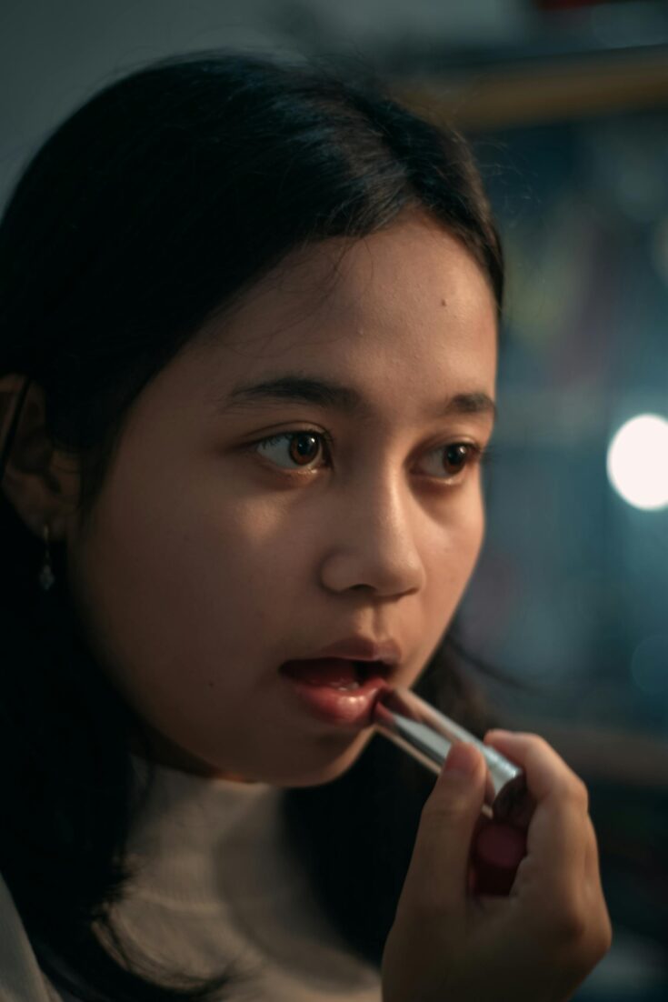 Young ethnic lady applying lipstick in dressing room