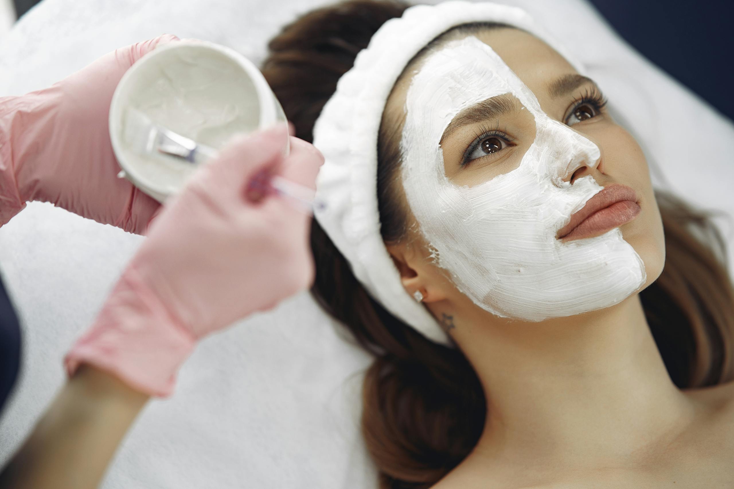 Crop unrecognizable beautician applying clay mask to clients face