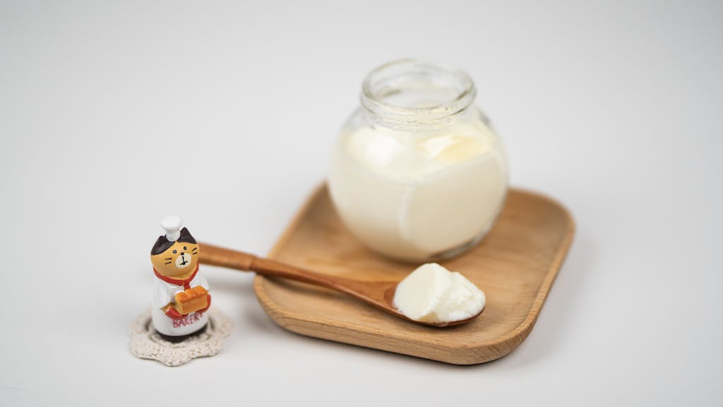 Jar with delicious plain yogurt and wooden spoon on saucer to make yoghurt clay mask for combination skin