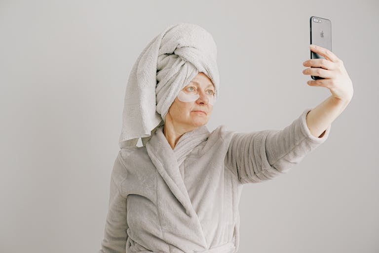 Woman in Gray Bathrobe Holding Black Smartphone